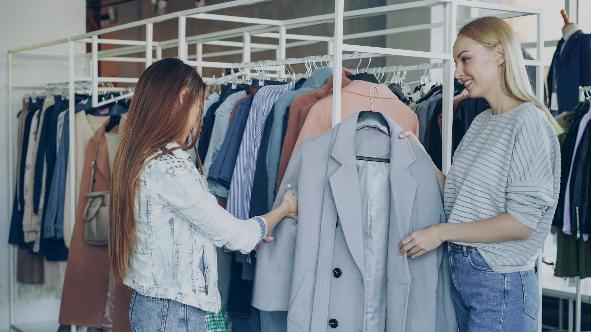 Two women choose clothes on a rail; one shows the other a coat