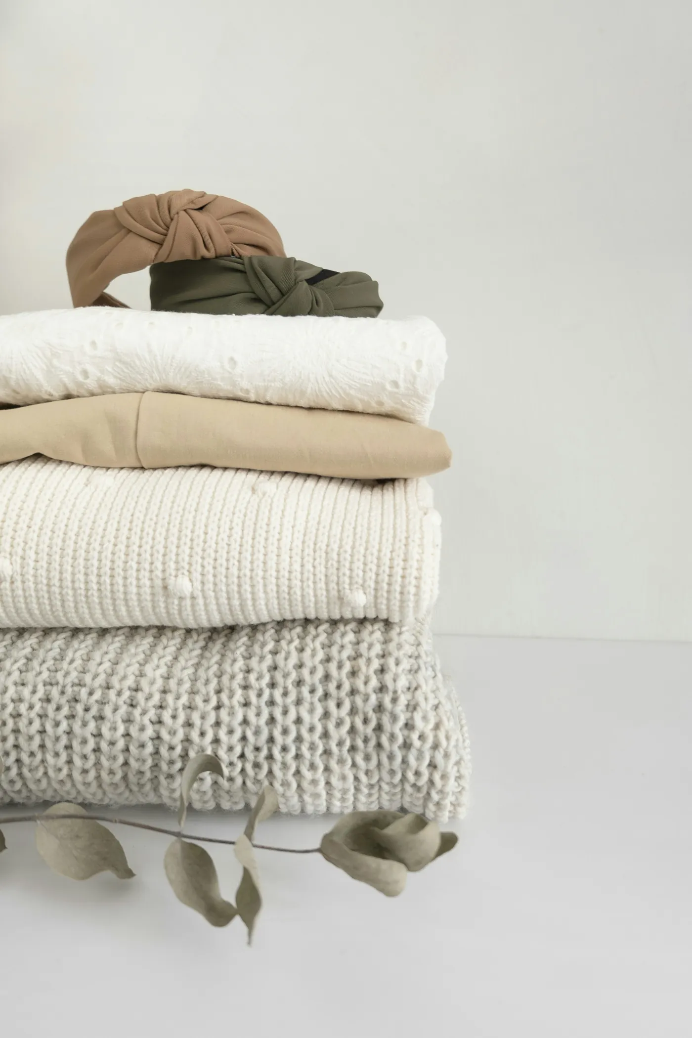 A small stack of folded knitwear in cream and beige, with a dried branch