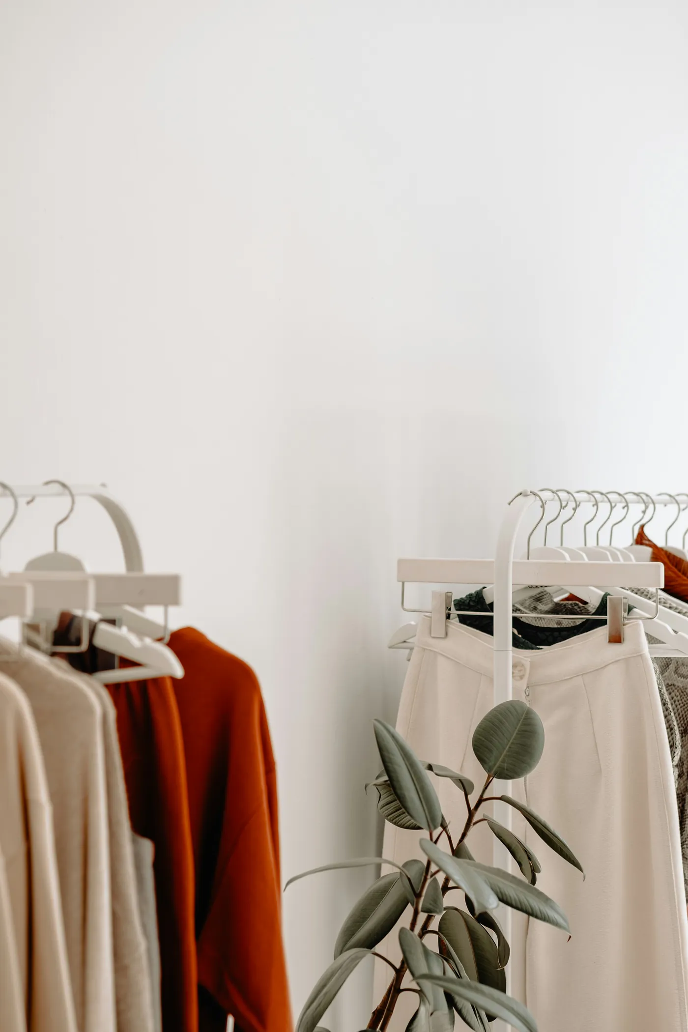 A tidy open wardrobe: a rail of neutral clothes, a round mirror and a hat
