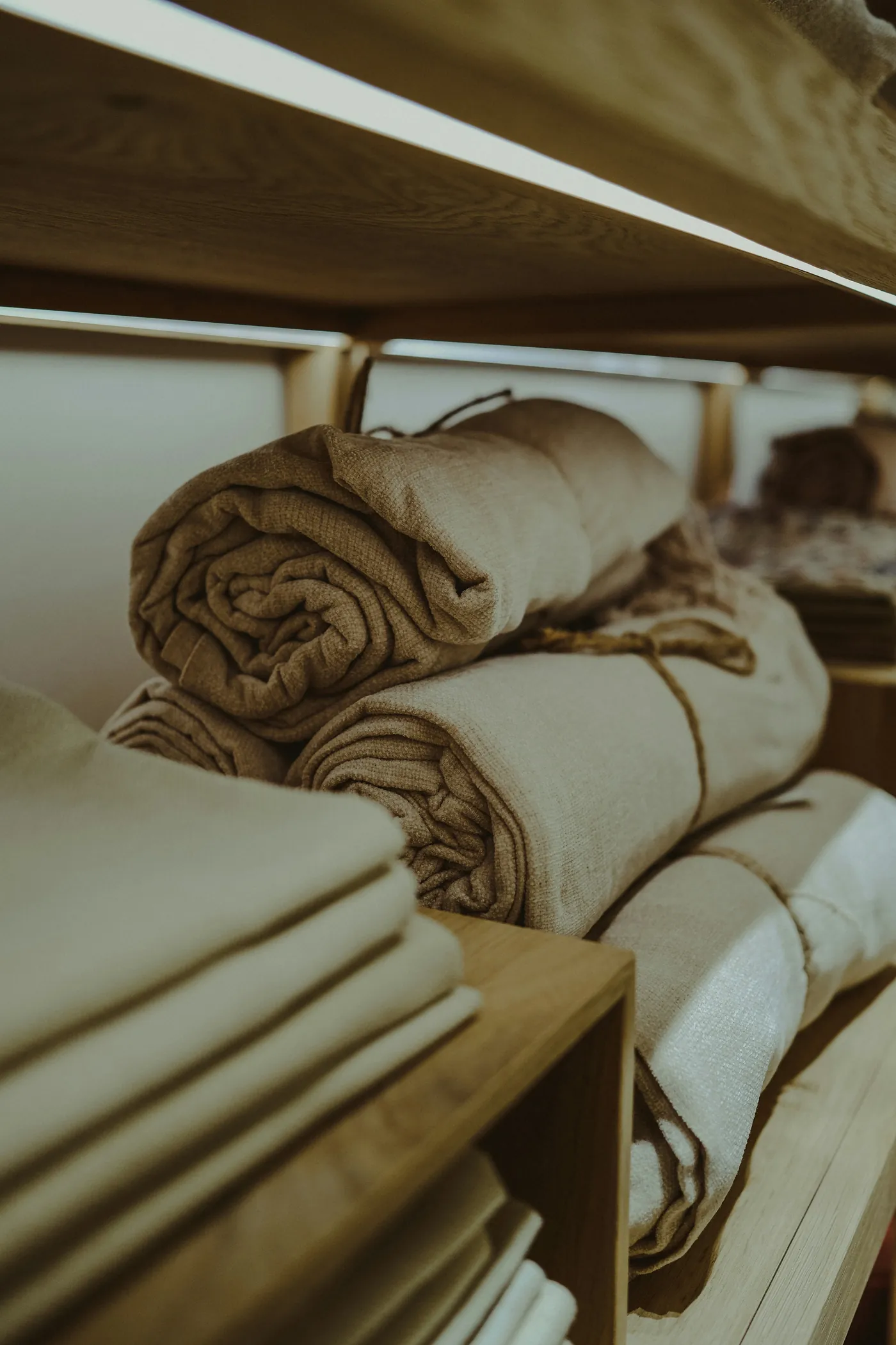 Linen folded and rolled on a wooden shelf, in warm light